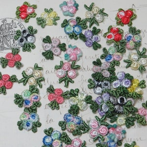 May include: Assortment of colorful embroidered flower embellishments with green leaves. The flowers are in various shades of pink, blue, red, yellow, and white.