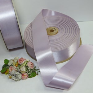 May include: A spool of lavender satin ribbon. The ribbon is wound around a cardboard spool and is ready to be used for crafting, decorating, or gift wrapping.