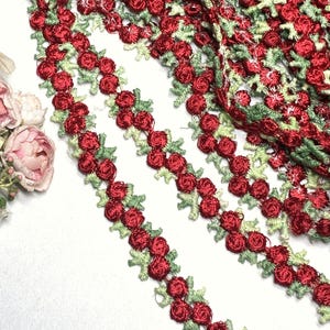 May include: Close-up of red rose trim with green leaves. The trim is made of a delicate, embroidered fabric. The roses are a deep red color, and the leaves are a light green. The trim is perfect for adding a touch of elegance to any project.