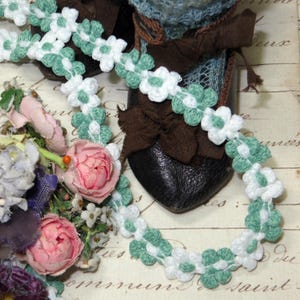 May include: White and green crocheted trim with a flower design. The trim is shown on a brown shoe with a lace top and a white background.