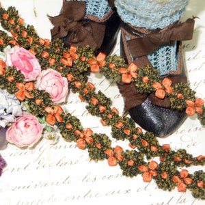 May include: Two strands of green and orange trim with a floral design. The trim is on a white surface with handwritten text.