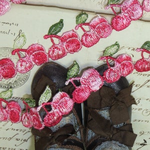 May include: Pink and white cherry embroidered trim with green leaves. The trim is shown on a pair of brown shoes with lace.