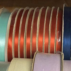 May include: A collection of spools of satin ribbon in various colors, including red, blue, and teal. The ribbons are neatly wound on cardboard spools, showcasing their smooth texture and vibrant hues. Ideal for crafts and gift wrapping.