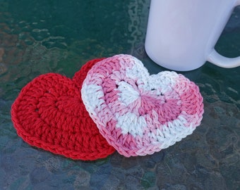 May include: Two heart-shaped crochet coasters. One is solid red, the other is a mix of pink, white, and light pink. A white mug is in the background. These handmade coasters are perfect for Valentine's Day or everyday use.