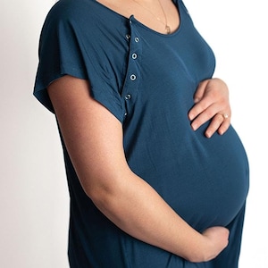 Puede incluir: Una persona embarazada lleva un vestido de maternidad azul teal con mangas cortas y un panel de acceso para lactancia. El vestido tiene un escote redondo y está hecho de una tela suave y elástica.