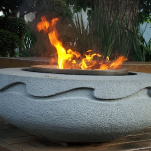 May include: A gray concrete fire pit with a wave design. The fire pit is filled with burning wood and flames.
