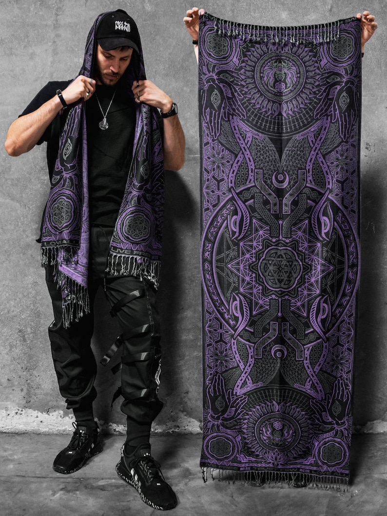May include: A black and purple shawl with a geometric design and fringe. The shawl is held up to display the intricate pattern. The design includes circles, lines, and symbols. The shawl is worn as a hood.