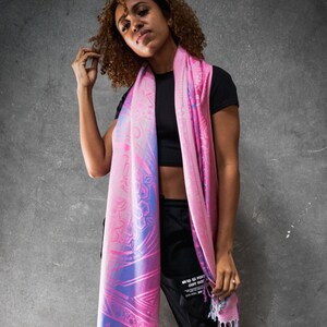 May include: A pink and blue patterned scarf with a fringe. The scarf is made of a soft, lightweight fabric and features a geometric design.