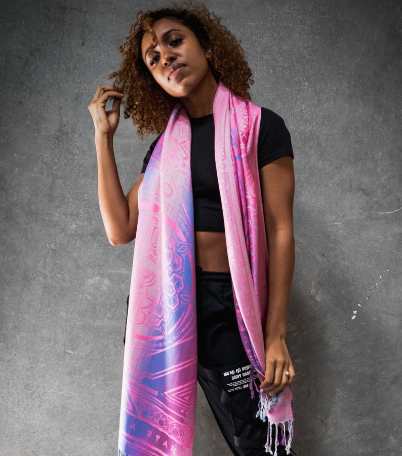 May include: A pink and blue patterned scarf with a fringe. The scarf is made of a soft, lightweight fabric and features a geometric design.