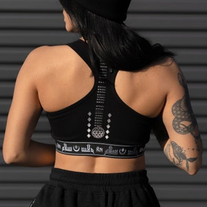 May include: Black sports bra with a silver geometric design on the back and the text "RN سلم الله" on the bottom band.