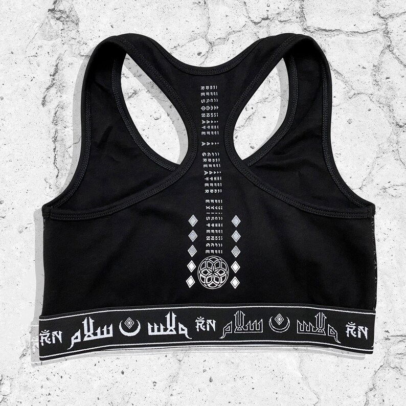 May include: Black sports bra with a white geometric design and the text "RN" and "SALAM" repeated on the bottom band.