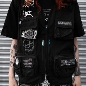 May include: Black utility vest with multiple pockets and zipper closures. The vest features graphic designs with text including "Rage Against The Machine" and "Convene Within The Elements To Change The World".