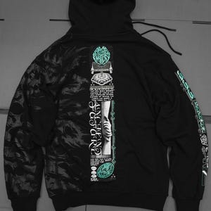 May include: Black hooded sweatshirt with a graphic print on the front and back. The front print features a hand holding a chain with the text "Ancient Code" and "Together" in a stylized font. The back print features a graphic with the text "Rage Against The Machine".
