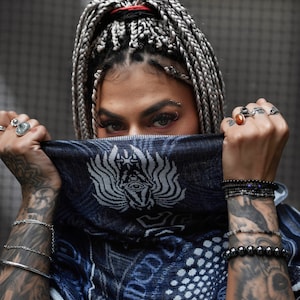 May include: A person with long, gray and black braids, wearing a blue bandana with a white design, and multiple bracelets on both wrists.