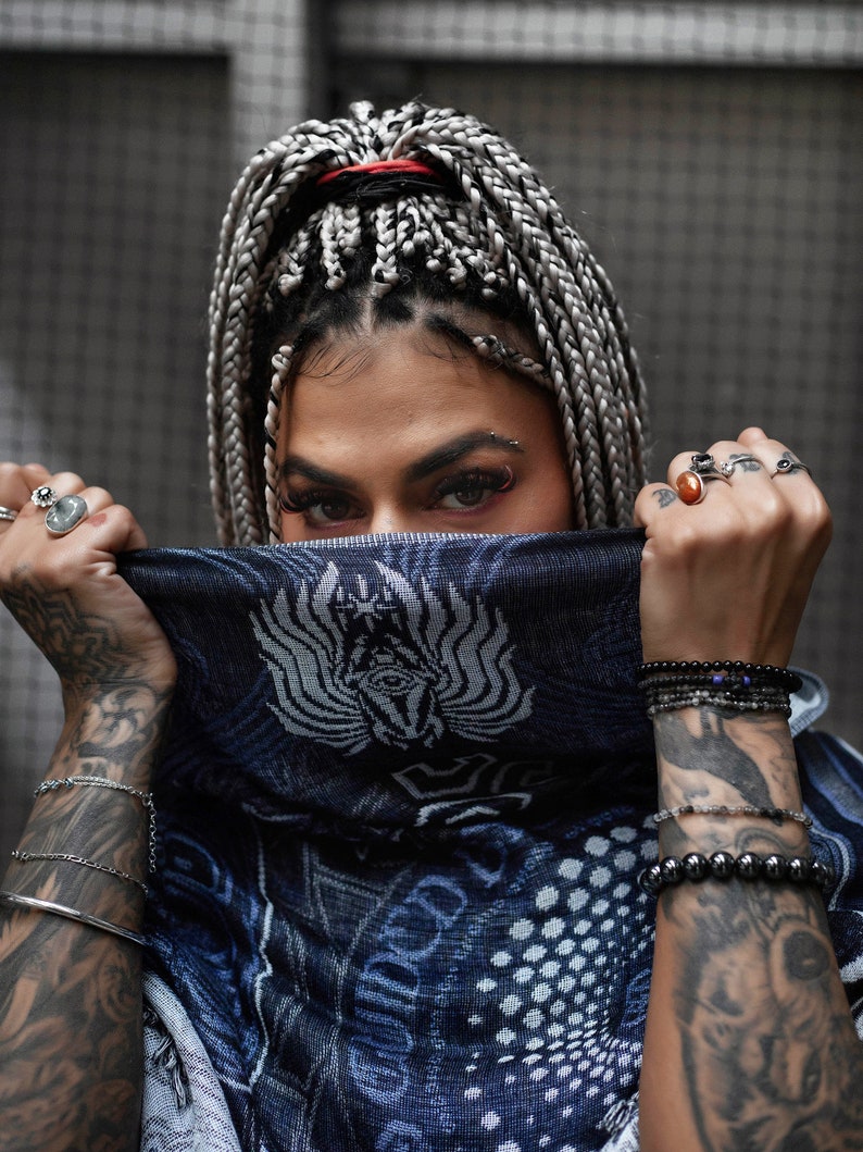 May include: A person with long, gray and black braids, wearing a blue bandana with a white design, and multiple bracelets on both wrists.