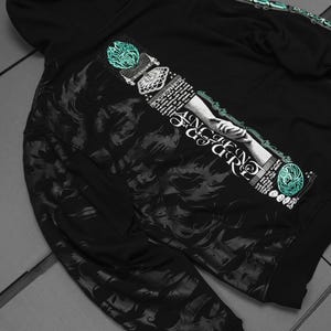 May include: Black hooded sweatshirt with a graphic print of a hand reaching out from a cloud with the text "ANCIENT FIGURE" and other text in a stylized font. The graphic is in shades of gray and teal.
