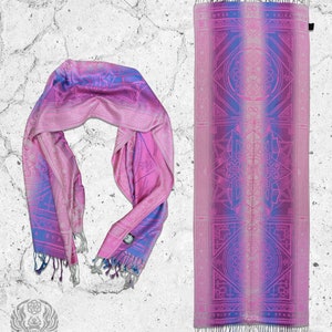 May include: A pink and blue patterned scarf with a geometric design. The scarf is folded and laid out on a white textured surface. The text "TRIZE RISE A STAND" is printed on the scarf.