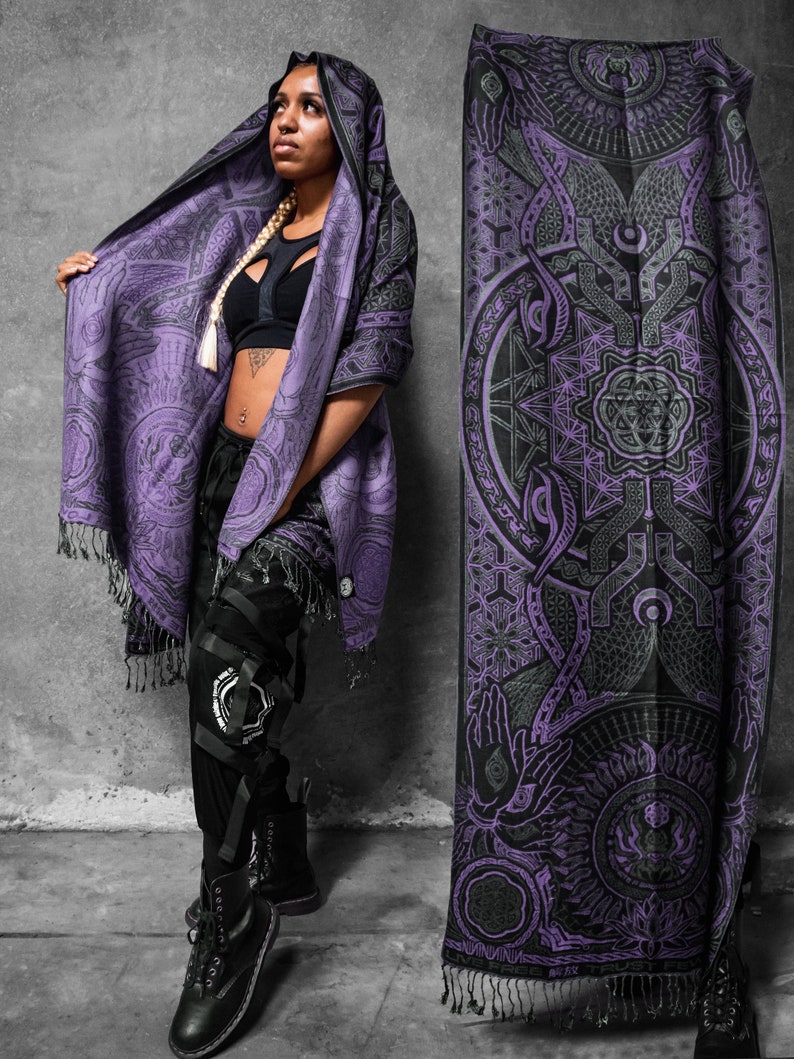 May include: A purple and black geometric patterned hooded shawl. The shawl has a detailed design and fringing. The person is wearing black trousers and boots.