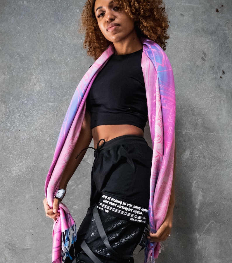 May include: A person wearing black pants with a graphic print and a pink and blue scarf. The pants have multiple straps and buckles. The text on the pants reads "JUST BE PATIENT IN THE GAME, SOME DON'T MAKE IT DIFFERENT TIMES."