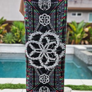 May include: A black tapestry with a geometric pattern. The design includes a large white floral motif, with red, green, and purple accents. The edges are finished with a fringe.