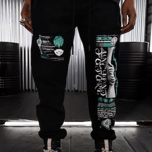 May include: Black sweatpants with a graphic print featuring a hand, chains, and text in green and white. The text includes "ANCIENT FUTURE" and "DOX TIME IS NOW".