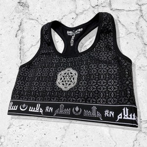 May include: Black sports bra with a white geometric pattern and a white circular design in the center. The bottom band has white Arabic script.