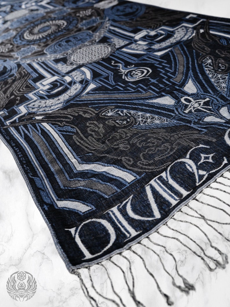 May include: A blue and gray patterned scarf with a fringe. The scarf has the word "DIVINE" woven into the fabric.