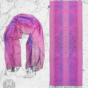 May include: A pink and purple patterned silk scarf with a geometric design. The scarf is folded in half and has a fringe on the ends. The scarf is laid out on a white textured background.