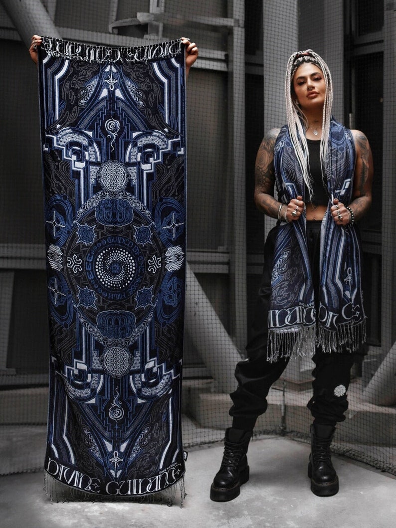 May include: A blue and black patterned scarf with fringe. The scarf features a geometric design with a circular mandala in the center. The text "Divine Guidance" is printed on the bottom of the scarf.