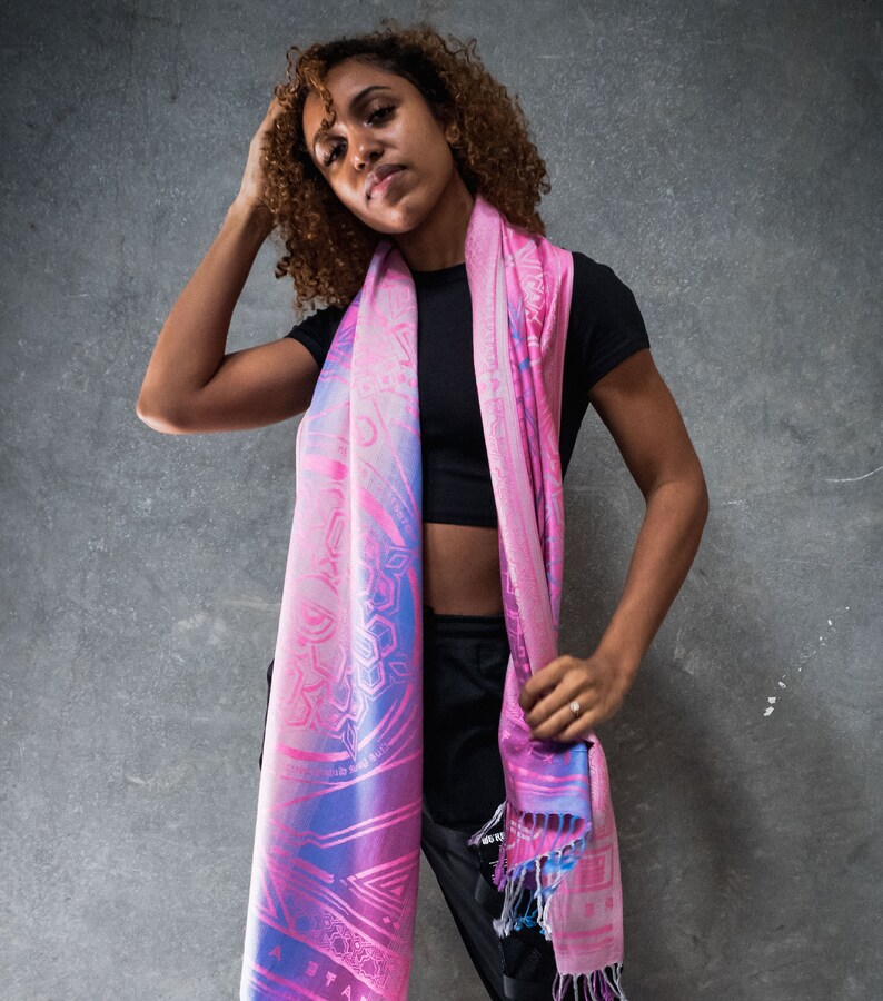 May include: A woman wearing a black top and black pants with a pink and blue patterned scarf. The scarf has a geometric design and is tied around her neck.