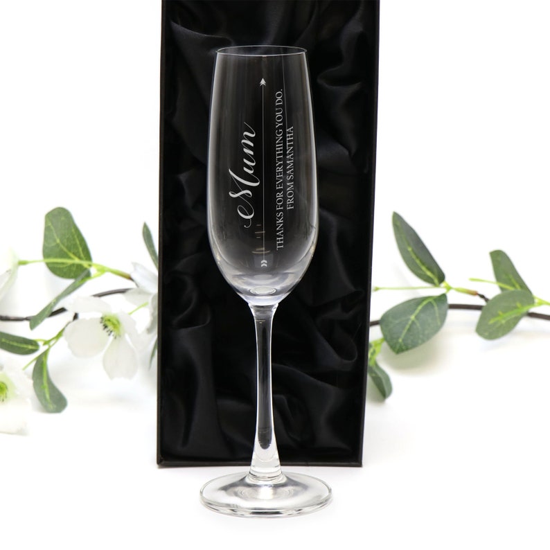 May include: A clear glass champagne flute with an engraved message that reads "To Mum, Thanks for everything you do. From Samantha". The flute is in a black velvet box.