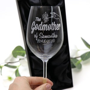 May include: A clear glass wine glass with an etched design that says "The Godmother of Samantha 24.10.2020".