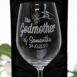 May include: A clear glass wine glass with an etched design that says "The Godmother of Samantha 24.10.2020". The design includes a hand holding a wand with sparkles.