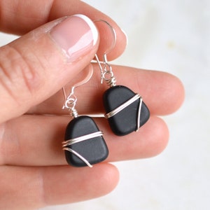 May include: A pair of black gemstone earrings with silver wire wrapping. The earrings are teardrop shaped and dangle from silver hooks.