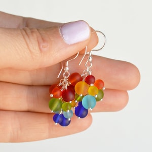 May include: Rainbow colored glass bead dangle earrings with silver hooks. The beads are arranged in a rainbow pattern, starting with red and ending with blue.