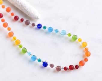 May include: A rainbow colored glass bead necklace with a silver wire thread. The beads are arranged in a gradient from red to orange, yellow, green, blue, and purple.