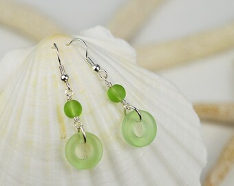 May include: A pair of silver dangle earrings with green glass beads and rings. The earrings are on a white seashell background.