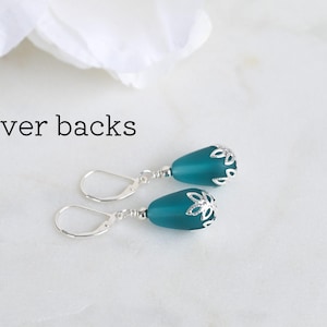 May include: Teal teardrop earrings with silver-colored lever backs. The earrings have a silver floral design at the top of the teal teardrop. The text "Lever backs" is above the earrings.