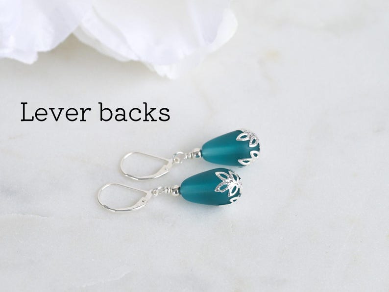 May include: Teal teardrop earrings with silver-colored lever backs. The earrings have a silver floral design at the top of the teal teardrop. The text "Lever backs" is above the earrings.
