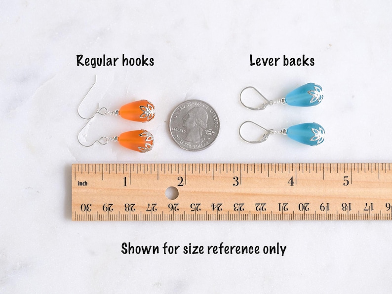 May include: Earrings with regular hooks and lever backs are shown for size reference. The orange earrings have a silver-colored floral design, while the blue earrings also have a silver-colored floral design. A ruler shows the earrings' size in inches.