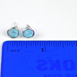 May include: A pair of silver stud earrings with light blue round glass stones. The earrings are shown next to a ruler, measuring approximately 1/2 inch in diameter.