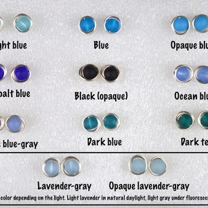 May include: A selection of glass beads in various shades of blue, teal, and gray, including light blue, blue, opaque blue, cobalt blue, black (opaque), ocean blue, opaque blue-gray, dark blue, dark teal, lavender-gray, and opaque lavender-gray. The beads are displayed on a white surface. The text "Change color depending on the light. Light lavender in natural daylight, light gray under fluorescent light" is written below the beads.