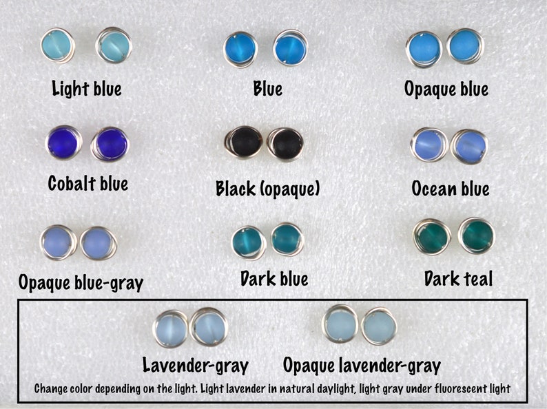 May include: A selection of glass beads in various shades of blue, teal, and gray, including light blue, blue, opaque blue, cobalt blue, black (opaque), ocean blue, opaque blue-gray, dark blue, dark teal, lavender-gray, and opaque lavender-gray. The beads are displayed on a white surface. The text "Change color depending on the light. Light lavender in natural daylight, light gray under fluorescent light" is written below the beads.