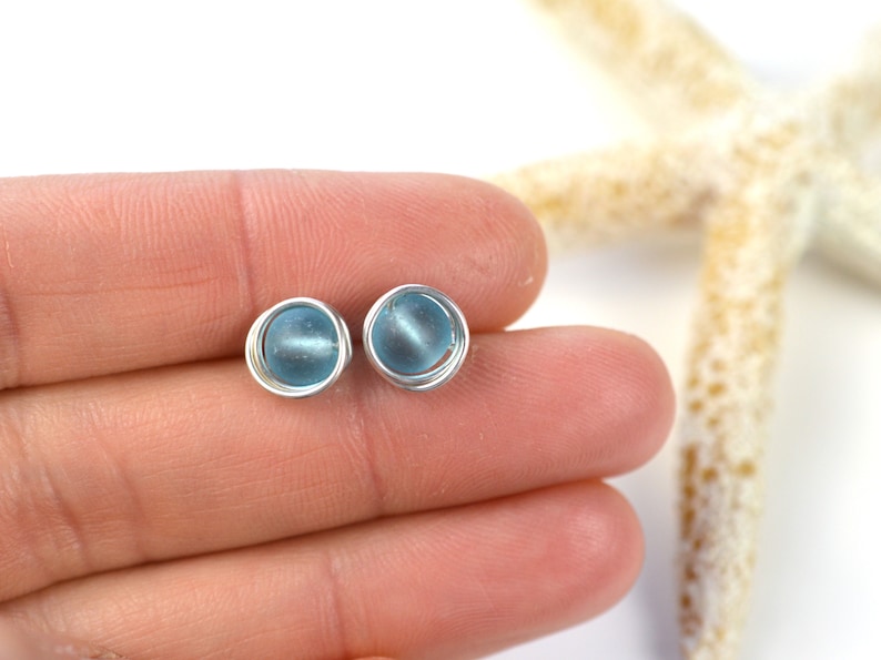 May include: A pair of silver wire wrapped earrings with light blue glass beads.