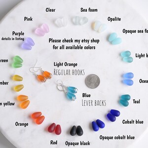 May include: A variety of colorful glass bead earrings and loose beads are displayed on a white surface. The beads come in various colors, including pink, purple, green, amber, orange, red, and blue. The image also shows text that says "Please check my etsy shop for all available colors."
