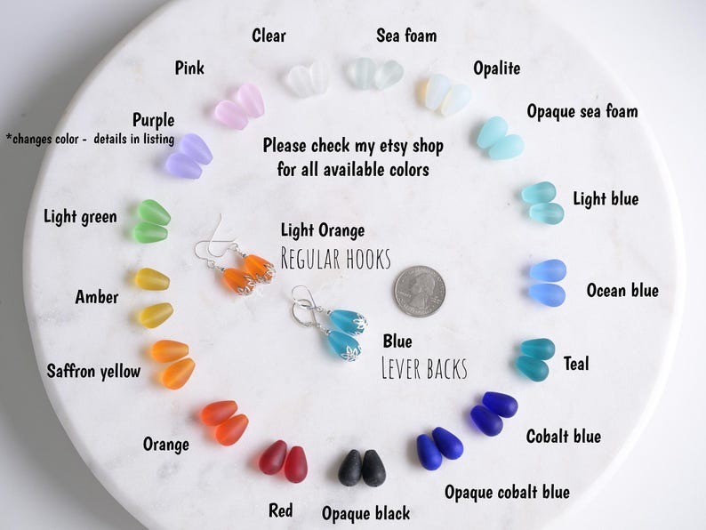 May include: A variety of colorful glass bead earrings and loose beads are displayed on a white surface. The beads come in various colors, including pink, purple, green, amber, orange, red, and blue. The image also shows text that says "Please check my etsy shop for all available colors."