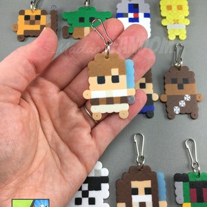 May include: A collection of pixel art keychains featuring various characters. The keychains are made of colorful beads and have silver-colored clasps. The image includes keychains of a character with a lightsaber, a green character, and a yellow character.
