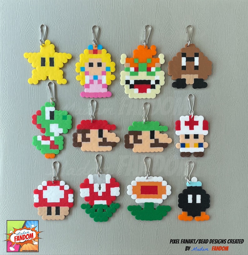 A variety of 12 handmade Super Mario Party Favors lay on a grey background. Each character has a metal lanyard hook attached to a jump ring.