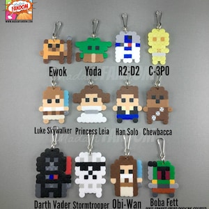 May include: A collection of Star Wars character keychains made from colorful beads. Characters include Ewok, Yoda, R2-D2, C-3PO, Luke Skywalker, Princess Leia, Han Solo, Chewbacca, Darth Vader, Stormtrooper, Obi-Wan, and Boba Fett. The keychains are attached to silver-colored clasps.