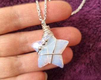 May include: A silver chain necklace with a wire-wrapped opal star pendant. The star is a light blue color and has a silver wire wrapped around it. There are small silver beads on the wire.